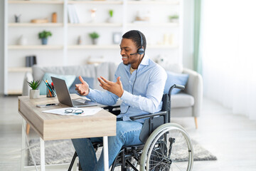 Disabled black guy with headset communicating online on laptop, having business meeting from home