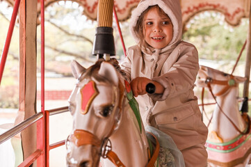 Fototapeta na wymiar The girl in bright clothes rides on the carousel on a holiday. Happy baby is having fun