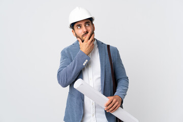 Young architect man with helmet and holding blueprints isolated on white background having doubts and with confuse face expression