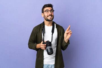 Photographer man over isolated purple background with fingers crossing and wishing the best