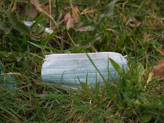 A used, blue surgical mask used for COVID-19 PPE protection, discarded as litter by a rural countryside hedgerow causing environmental pollution