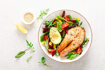 Salmon fish steak grilled, avocado and fresh vegetable salad with tomato, bell pepper and leafy vegetables. Top view