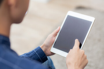 Closeup young asian man sitting and using mockup of tablet computer with display blank screen on sofa at home, male holding digital tablet watch entertainment at living room, communication concept.