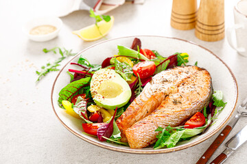 Salmon fish steak grilled, avocado and fresh vegetable salad with tomato, bell pepper and leafy vegetables