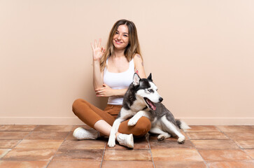 Young pretty woman with her husky dog sitting in the floor at indoors showing ok sign with fingers