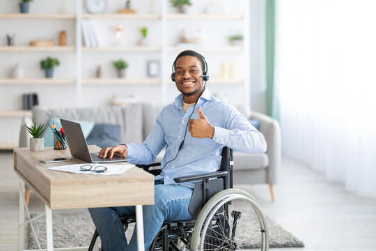 Positive Disabled Black Man In Headset Using Laptop Computer For Online Work, Showing Thumb Up Gesture At Home