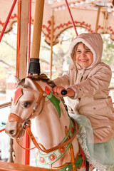 Fototapeta na wymiar The girl in bright clothes rides on the carousel on a holiday. Happy child has fun in the amusement park