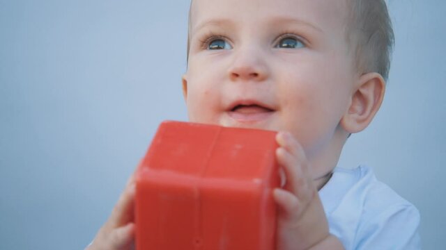 Close-up of a happy kid's face. A cute baby sits in a bright room, plays with cubes on a white background. The child plays with a colorful cube. child face with toy cube. happy family