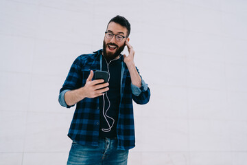 Millennial man in classic eyewear checking shocked publication news browsed on modern smartphone...