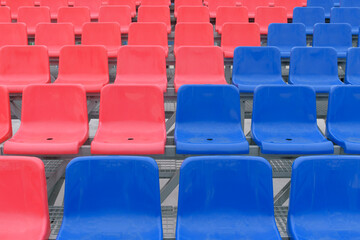 Rows of empty seats in the stadium. Plastic seats in red and blue. Diagonal symmetry.