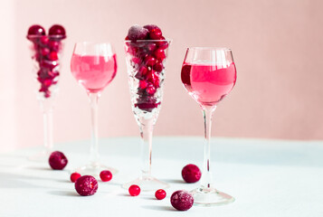 Fototapeta na wymiar a glasses of pink gin infused with cranberry among crystal glasses of berries on light background, a row of cherry liquor or any red alcoholic cocktail, minimal still life