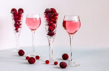 Fototapeta na wymiar a glasses of pink gin infused with cranberry among crystal glasses of berries on light background, a row of cherry liquor or any red alcoholic cocktail, minimalism