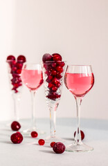 a glasses of pink gin infused with cranberry among crystal glasses of berries on light background, a row of cherry liquor or any red alcoholic cocktail, minimalism