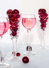 Fototapeta na wymiar a glass of pink gin infused with cranberry among crystal glasses of berries on white background, cherry liquor or any red alcoholic cocktail closeup