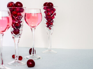 a glass of pink gin infused with cranberry among crystal glasses of berries on light background, cherry liqueur or any red alcoholic cocktail, copy space