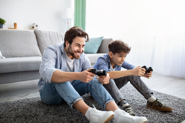 Joyful father and son competing in online video games, using joysticks, having fun at home.