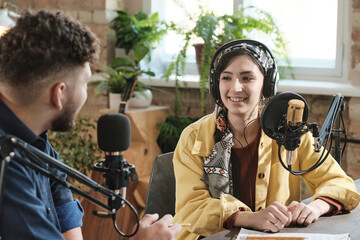 Young woman in headphones giving an interview to young man during broadcasting at radio studio