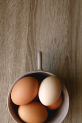 Ceramic bowl filled with fresh free range eggs on wooden table. Flat lay.