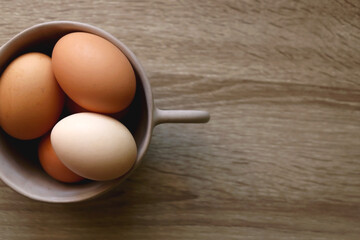 Ceramic bowl filled with fresh free range eggs on wooden table. Flat lay.