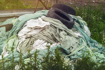 heap of old plastic tarpaulins weighed down with two car tires in nature