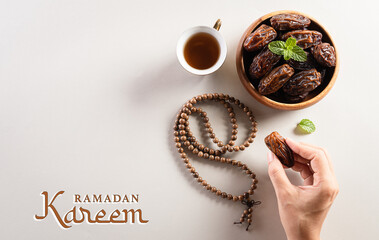 Ramadan Kareem background concept,  Hands picking up dates fruit, tea and rosary beads. Flat lay background with Ramadan text.