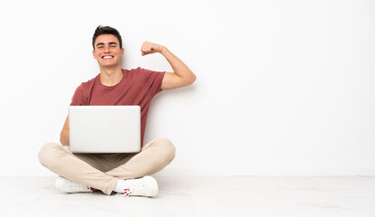Teenager man sitting on the flor with his laptop doing strong gesture