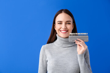 Young woman with teeth color chart on blue background
