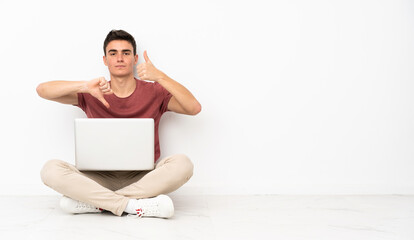 Teenager man sitting on the flor with his laptop making good-bad sign. Undecided between yes or not