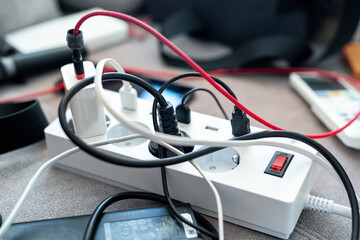 Overloaded power socket plug extendion at home. Tangled cords of home appliances and chargins...
