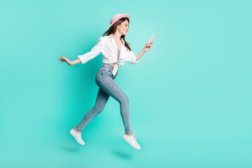 Fototapeta na wymiar Photo of adorable pretty young lady wear white shirt headwear jumping high looking modern gadget isolated turquoise color background