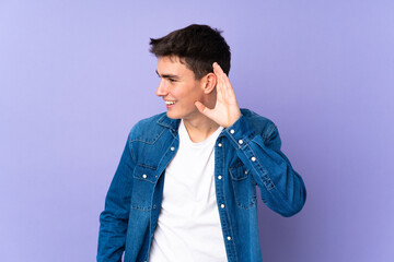 Teenager caucasian  handsome man isolated on purple background listening to something by putting...