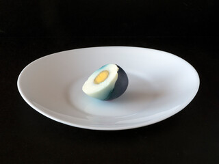 Easter egg, cut in half in a blue shell on a white plate on a black background.