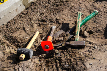 Defocus hammer, mallet, chisel and bayonet of the shovel lie on the ground. Set of tools for laying paving stones. Working process. Preparing to lay your patio with stone. Footprints. Out of focus