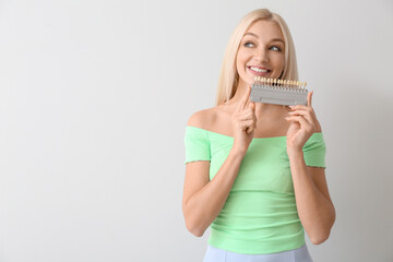 Young woman with teeth color chart on light background