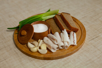 large horizontal photo. Snacks of lard, garlic, bread and green onions on a wooden board. Pork bacon with rye bread. Supplement to Ukrainian borscht. Vitamins. Prevention of colds. Salt. © Екатерина Тимошенко
