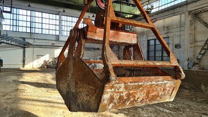 Rusty grab bucket or clamshell hanging on overhead crane in empty industrial plant.