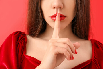 Naklejka premium Young woman with finger on lips, silence and secrecy concept, privacy and quiet gesture, red lipstick and velvet dress