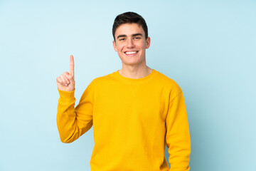Teenager caucasian handsome man isolated on purple background showing and lifting a finger in sign of the best