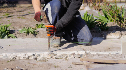 Defocus bricklayer removing irregularities on floor screed with hammer and chisel. Male hands in red work gloves smash the concrete slab. Out of focus