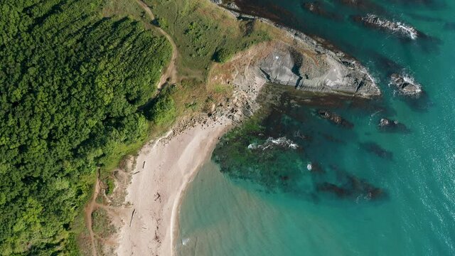 Drone flight above a picturesque rocky coastline with wild beaches, green forests and turquoise sea waters. Top view.