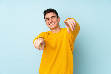 Teenager caucasian handsome man isolated on purple background points finger at you while smiling