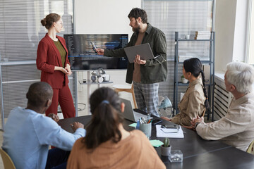 Portrait of modern bearded businessman giving presentation in office to IT team and pointing at code on screen, copy space