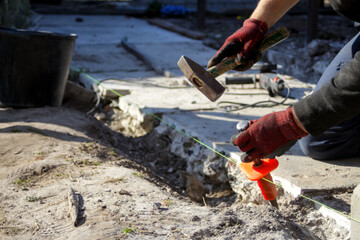 Defocus construction worker. Male hands in red work gloves hold a hammer and chisel. The paver...