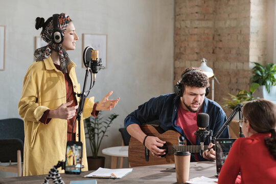 Musical group playing guitar and singing song and performing during air on radio with radio dj sitting opposite them