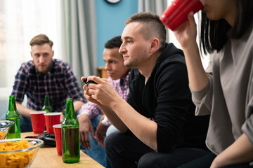 Group of friends play video games together at home, having fun. A focused man competes with a friend in his favorite video game.