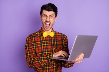 Photo of young crazy angry furious mad man in glasses having problem while working in laptop isolated on violet color background
