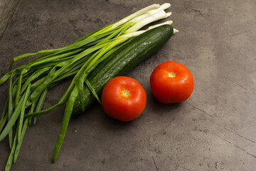 Obraz na płótnie Canvas fresh vegetables tomatoes, cucumber and greens on a dark stone background