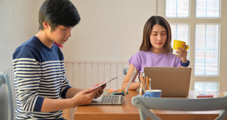 Female and male college students holding coffee mug and tablet with serious poses.