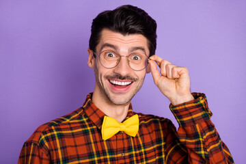 Photo of amazed young guy fingers eyeglasses look camera wear bow tie checkered shirt isolated purple background