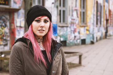 pierced and inked young woman in front of run-down graffiti covered houses